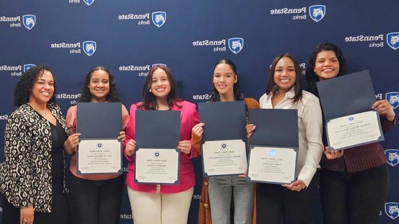 Five students hold certificates open with a staff member, all standing in front of a branded Penn State banner